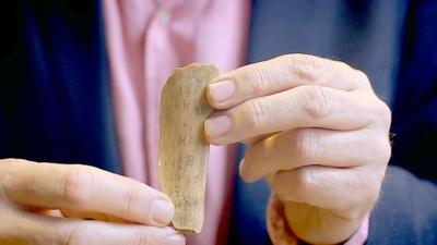 man holding a piece of bone with Chinese characters etched into it