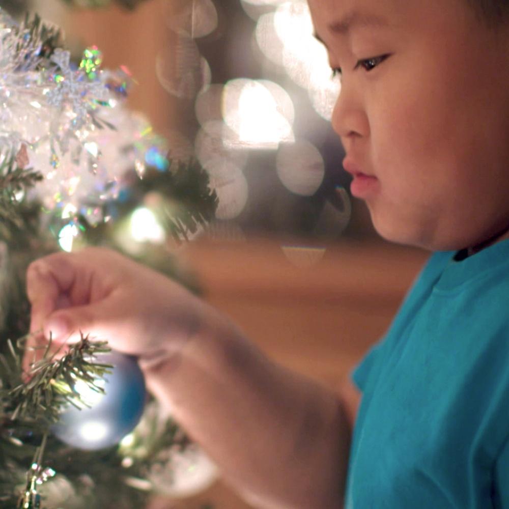 A closeup shot of a child hanging an ornament on a Christmas tree.