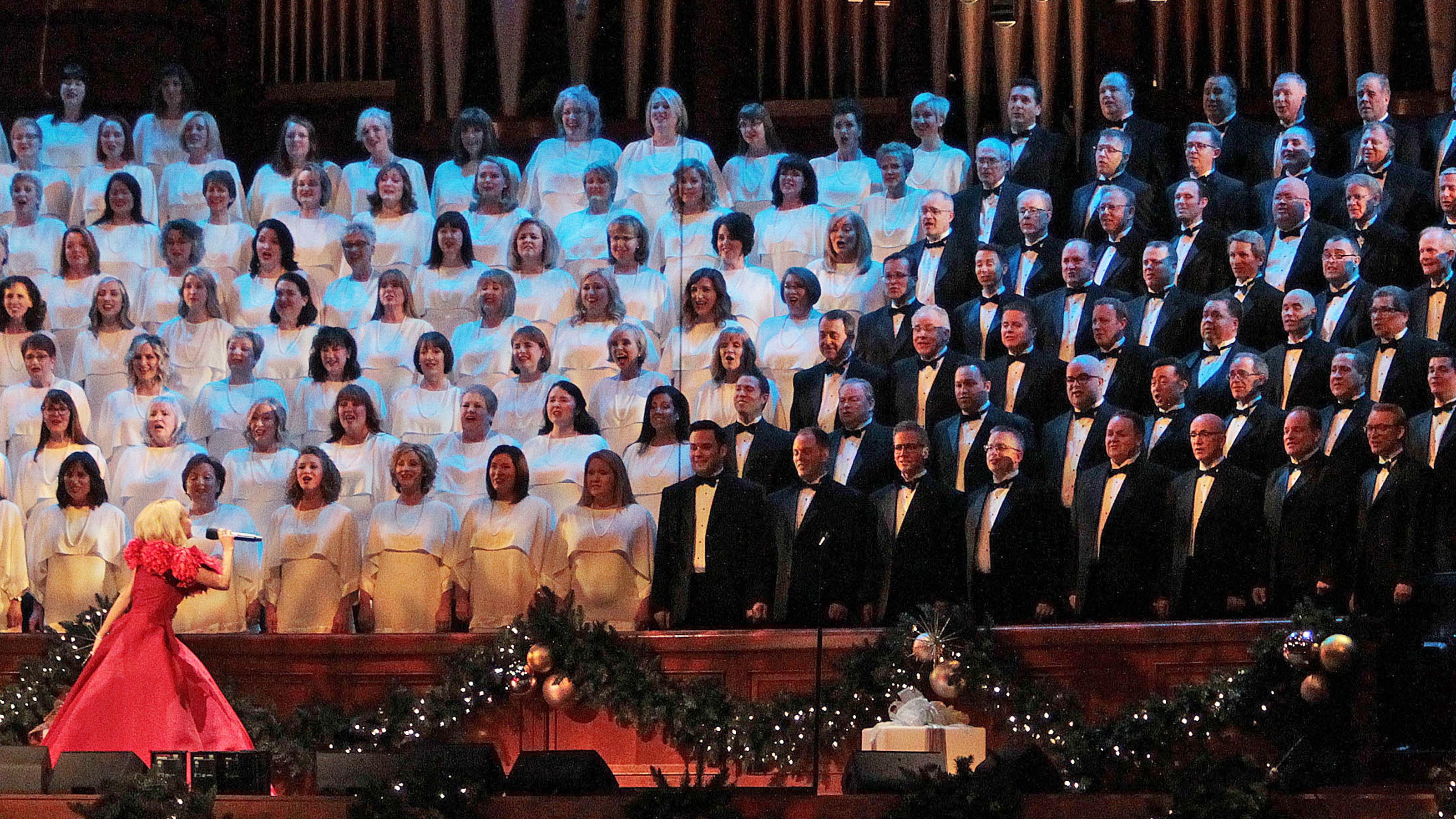 Kristin Chenoweth sings into a microphone while facing The Tabernacle Choir.