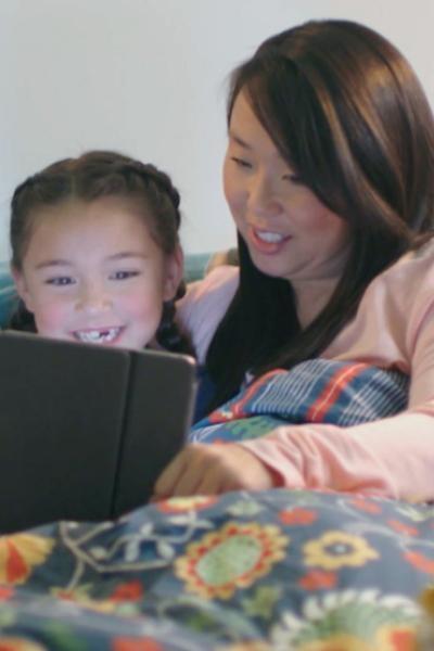A woman and young girl under a blanket watch Luke 2: The Christmas Story on a tablet.