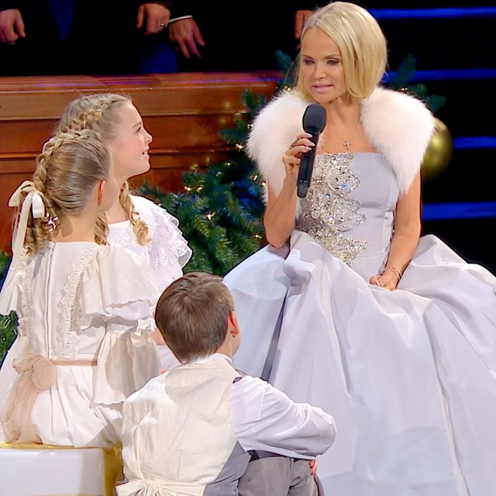 Sitting beside three children, Kristin Chenoweth sings What Child Is This? into a microphone.