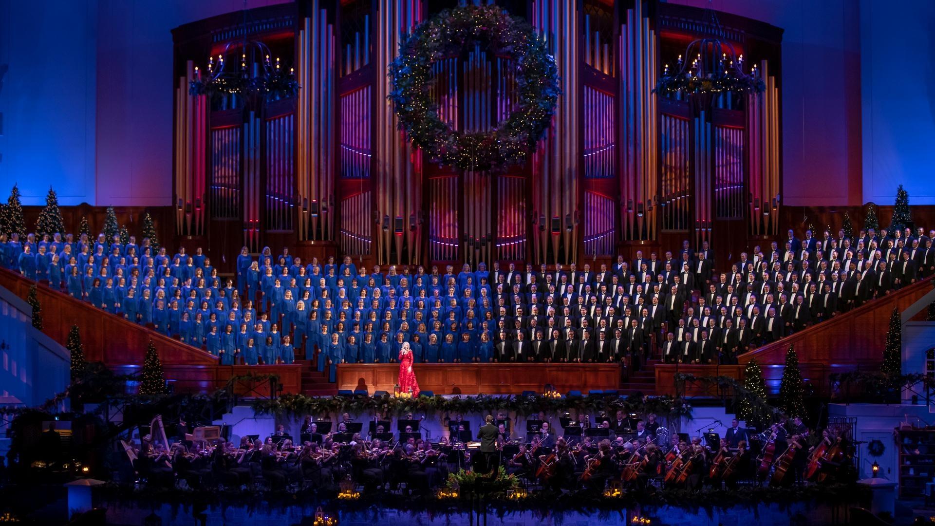 Kristin Chenoweth smiles on stage in front of a microphone with violinists playing behind her.