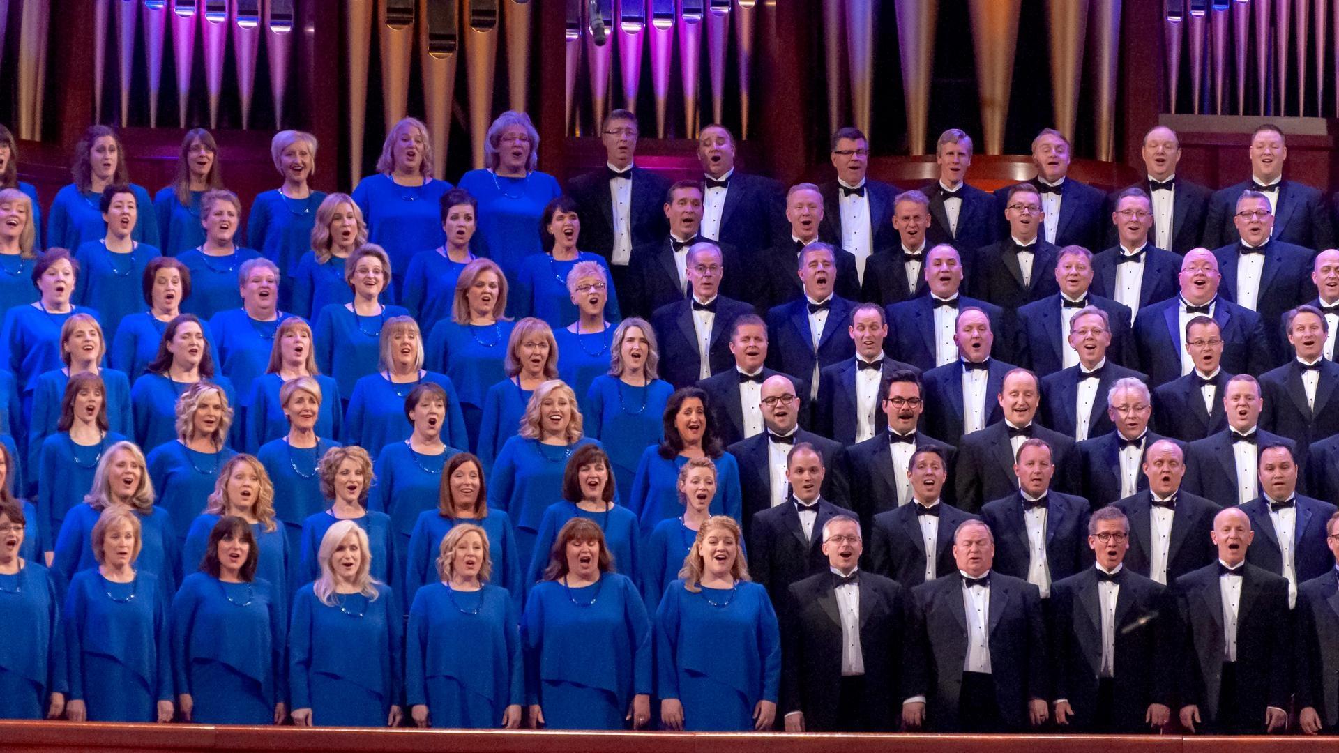 Female members of The Tabernacle Choir singing with Christmas decorations and a pipe organ behind them.