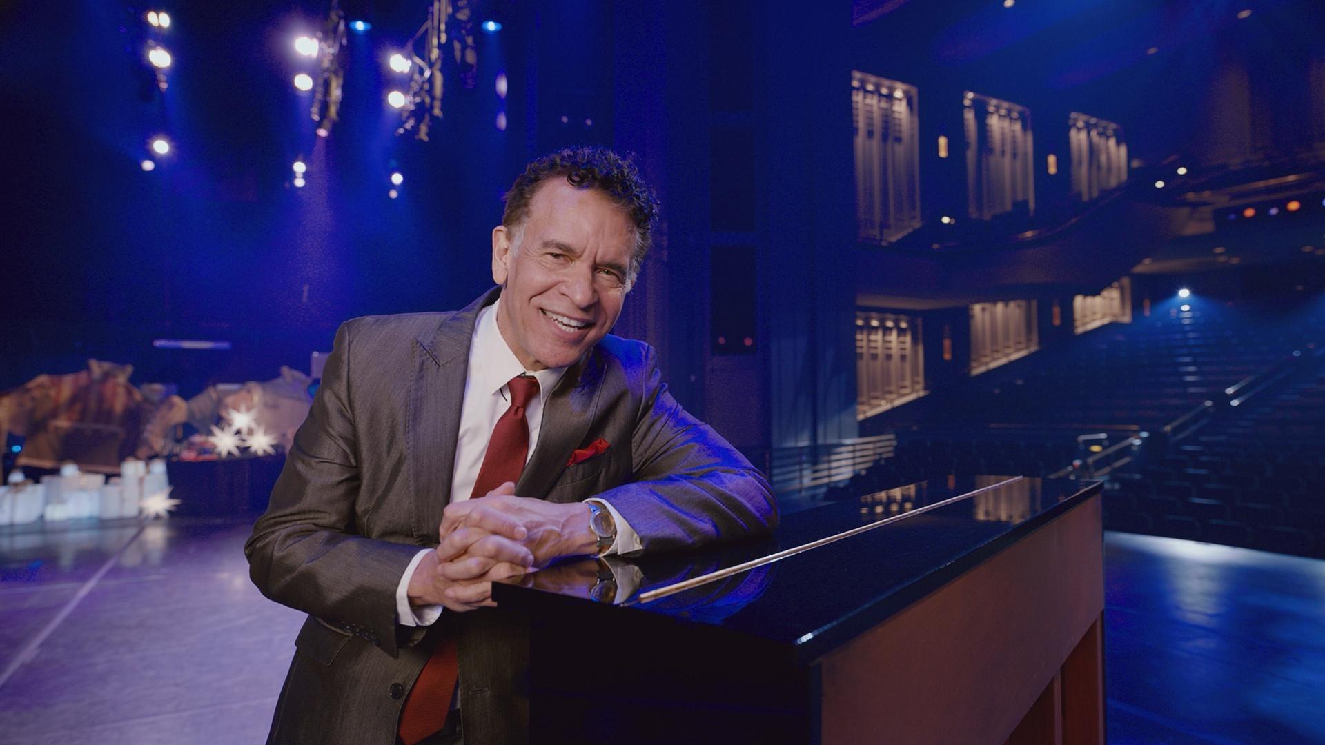 Brian Stokes Mitchell leans on a piano