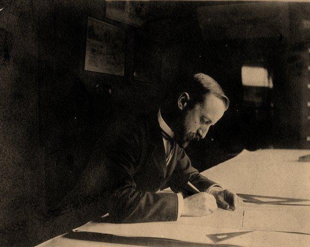 John Charles Olmsted sitting at a desk writing on a piece of paper.