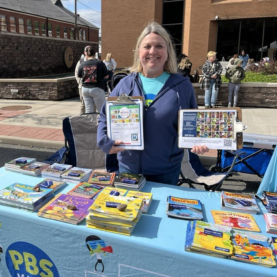 WBGU Director of Education and Outreach Kelly Pheneger hold an INFOhio Scholastic BookFlix Flyer and Who Would Win Choice Board Flyer at the Defiance Lilac Festival in Defiance, Ohio. WBGU distributed INFOhio Resources and children's books to families in attendance.
