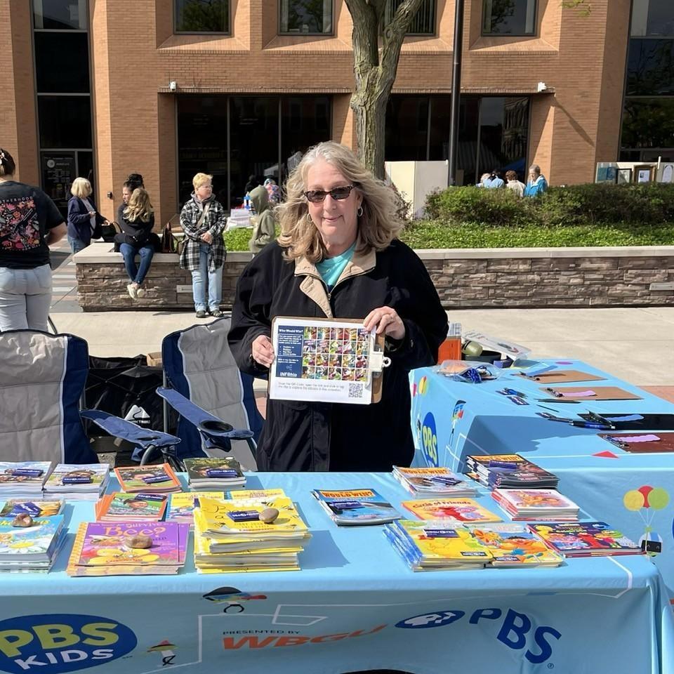 WBGU-PBS Membership Services Coordinator Cari Tuttle holds an INFOhio Who Would Win Choice Board Flyer at the Defiance Lilac Festival in Defiance, Ohio on May 9, 2026. WBGU distributed INFOhio Resources and children's books to families in attendance.