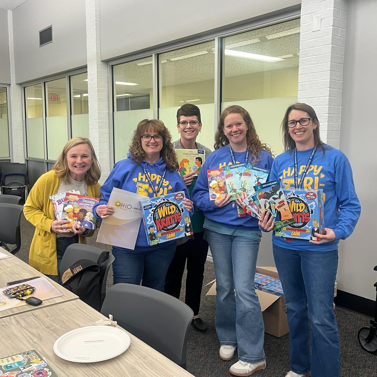  Hancock County Early Childhood Education Workgroup members in blue and yellow shirts smile and hold up Wild Kratts Board Games and Children's Books they received at a WBGU training on April 10, 2026
