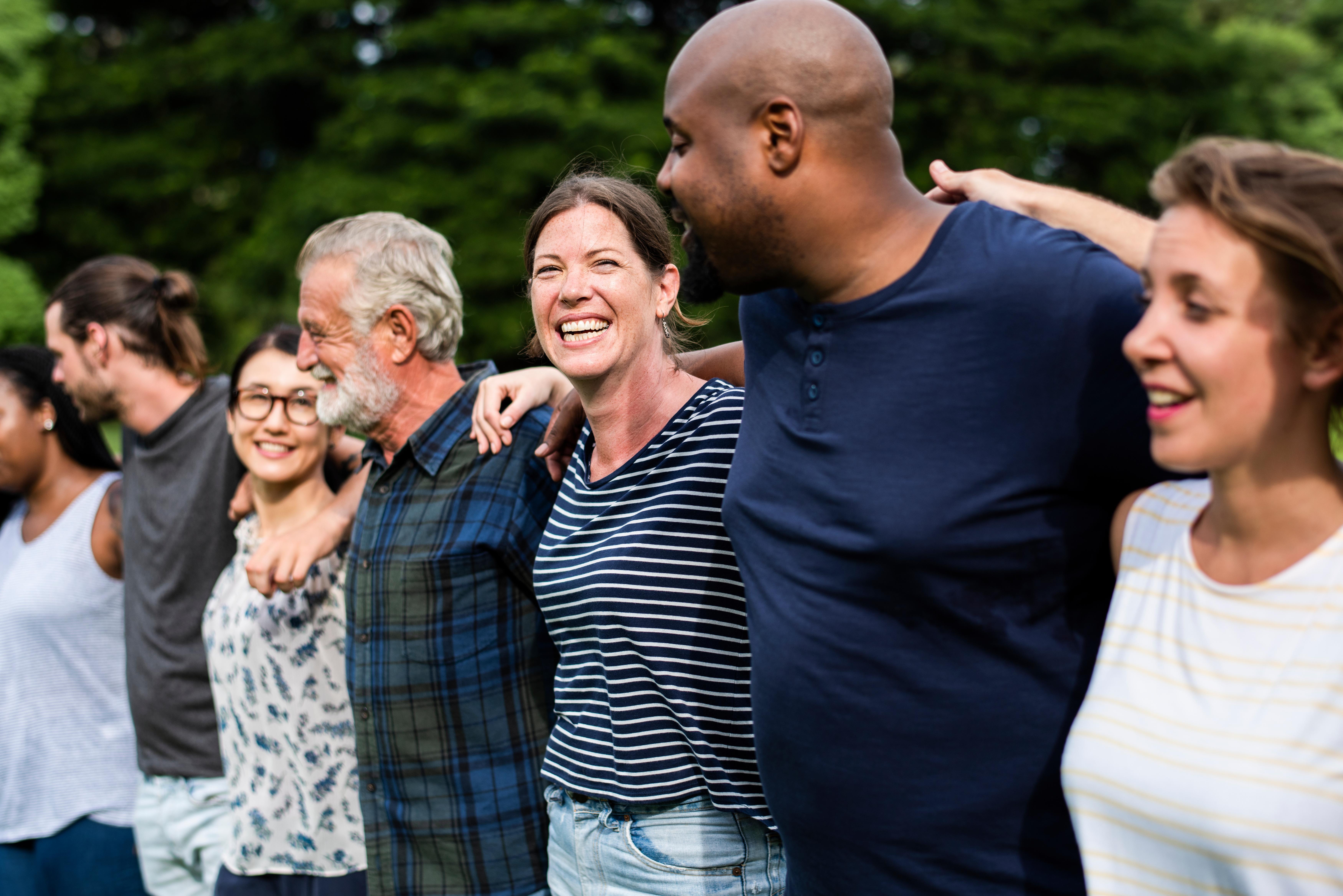This image shows a diverse group of people standing together in a park, smiling and celebrating. 