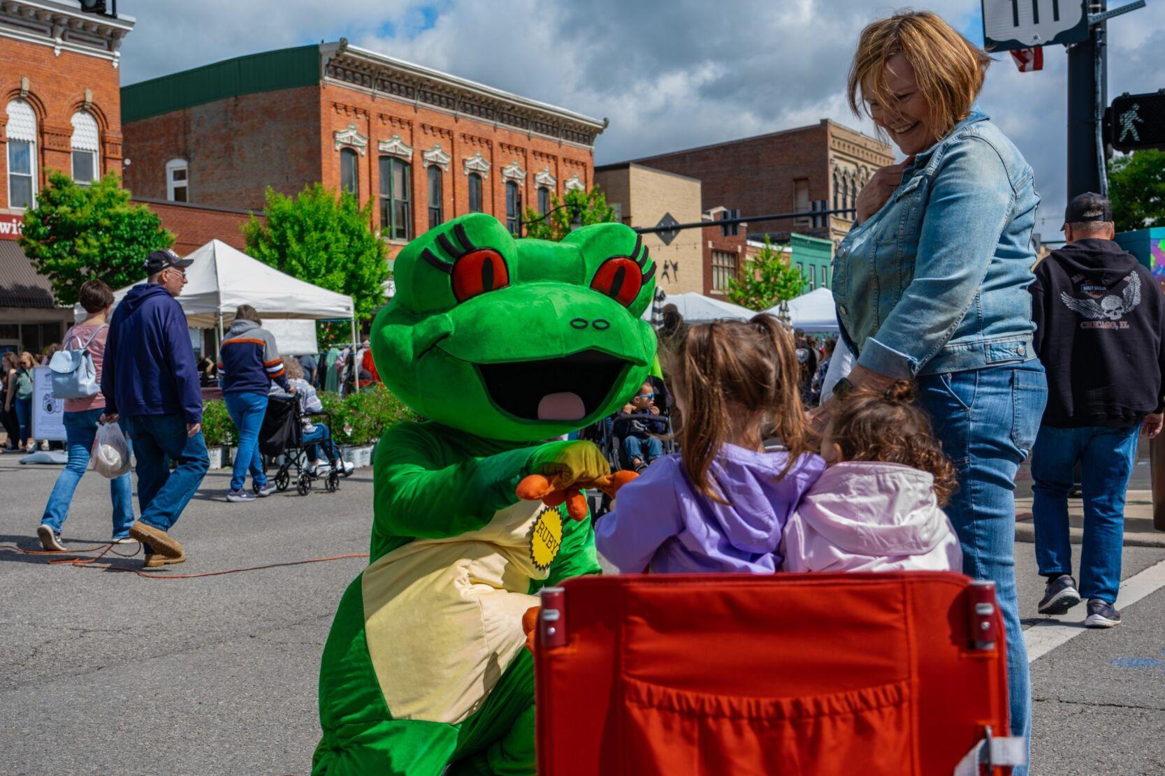 Station mascot Ruby the Red-eyed Tree Frog giving 2 girls in a wagon a fist bump