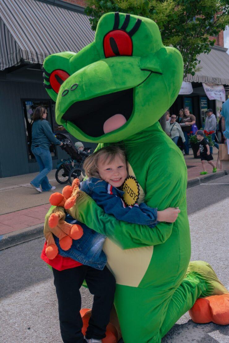 Girl getting a hug from station mascot Ruby the Red-eyed Tree Frog