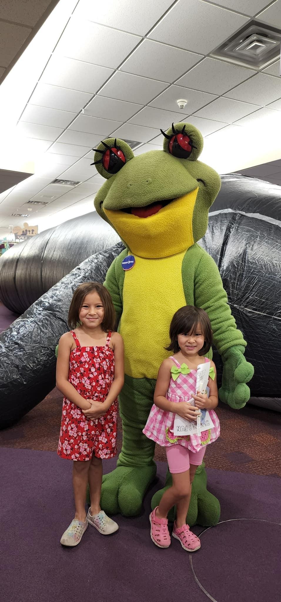 2 girls with Station mascot Ruby the Red-eyed Tree Frog standing by inflatable whale