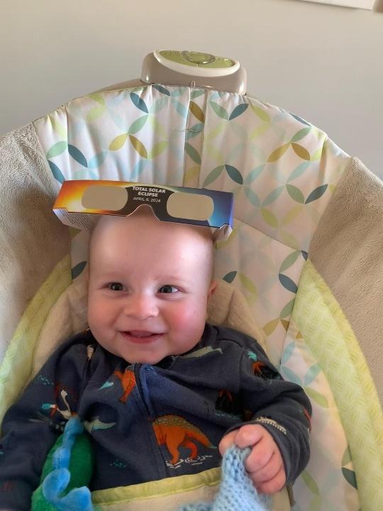 Baby smiling with solar eclipse glasses on his head