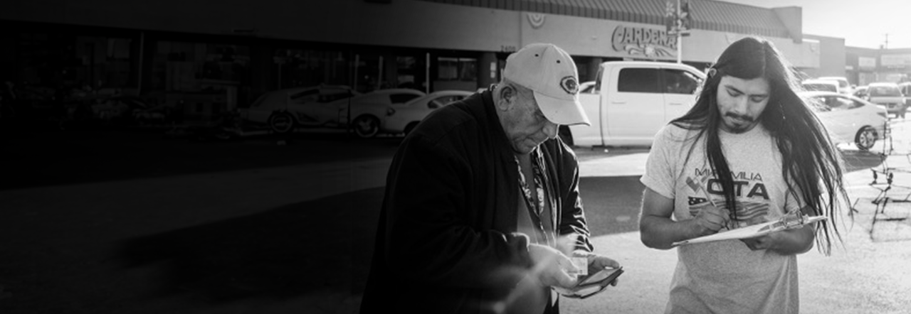 A young person with long hair assists an older person in registering to vote