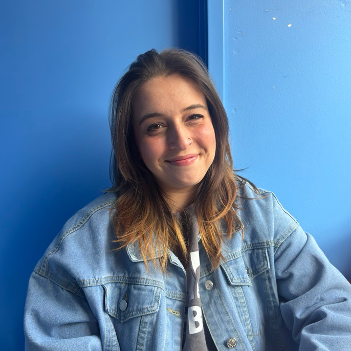 Image of woman in a denim jacket smiling with a blue background