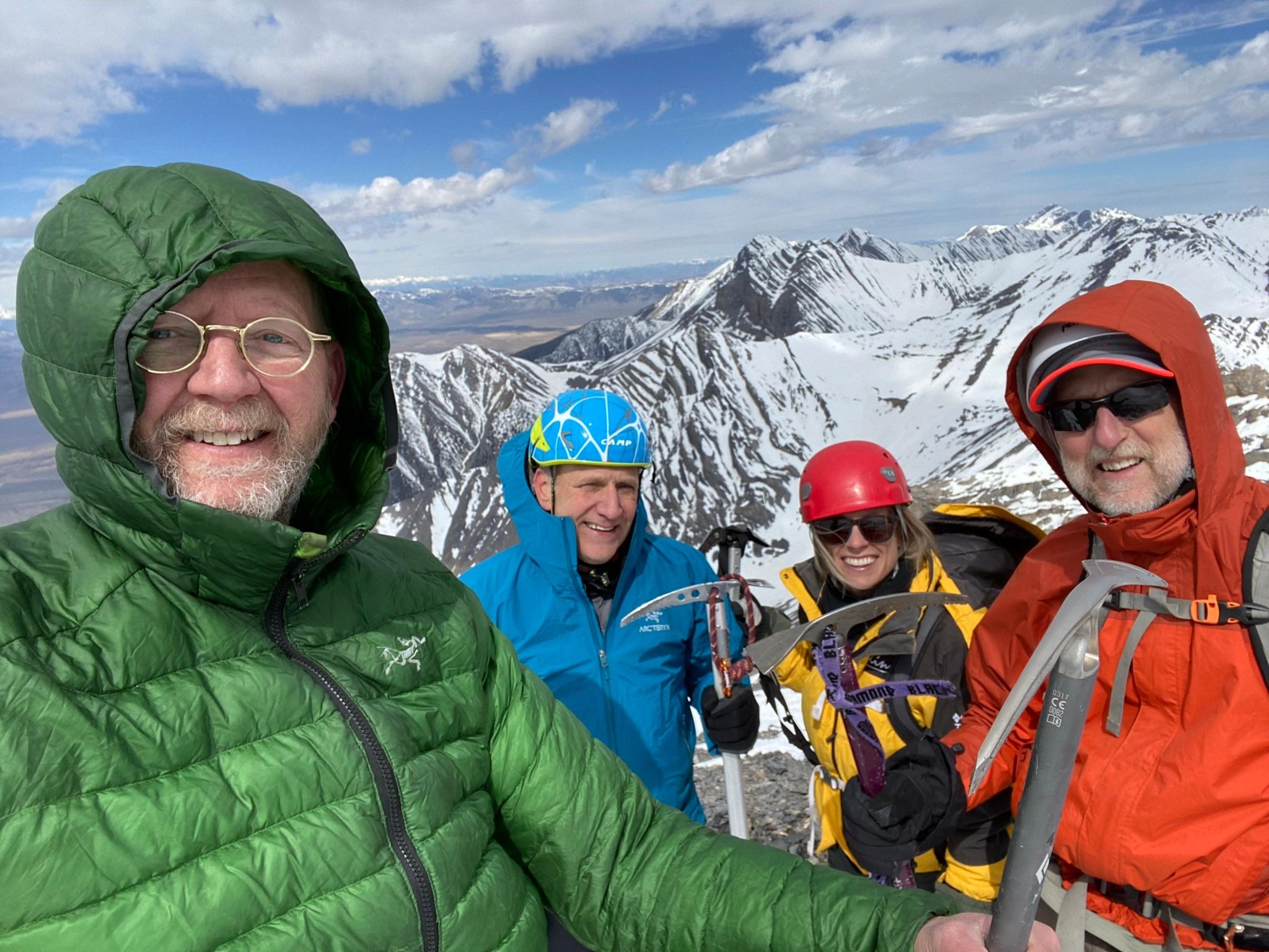 Four people smiling in heavy coats at the top of a mountain