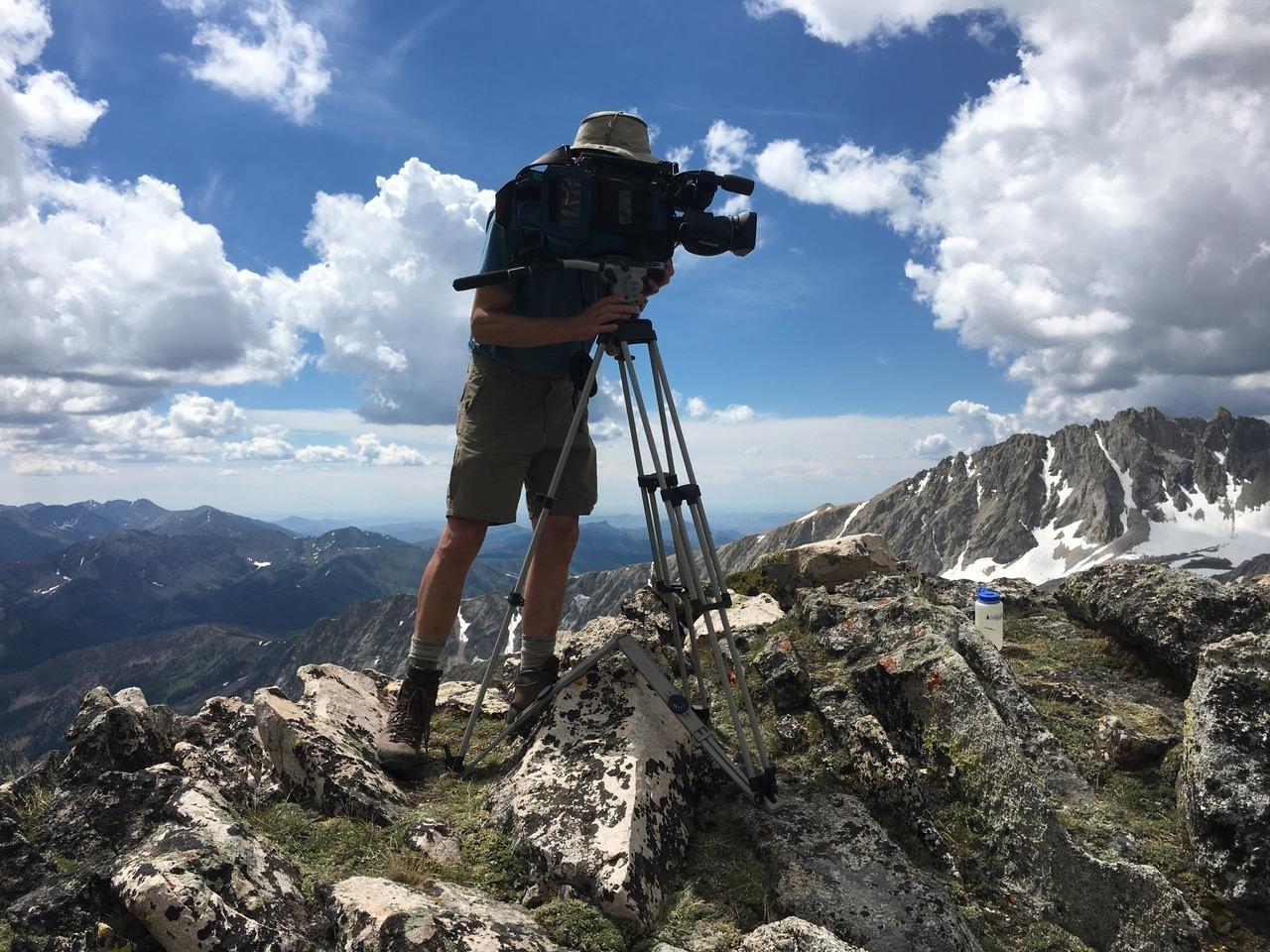 Man looking through video camera on top of mountain