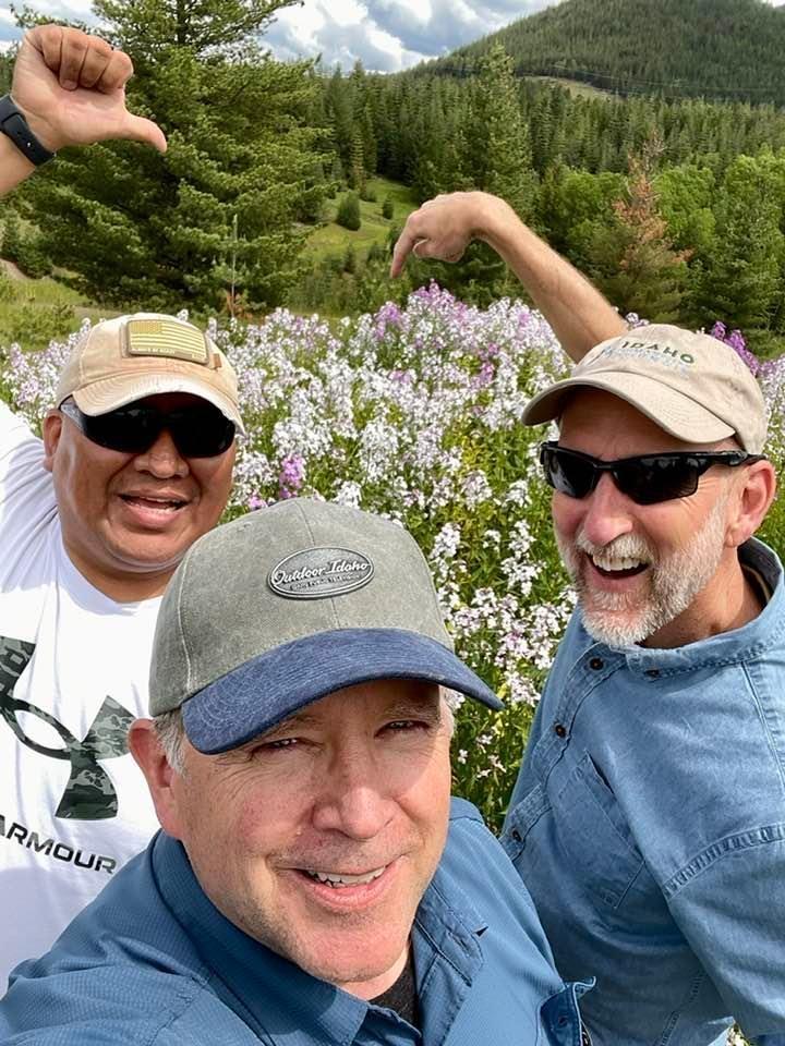 Three men pointing at a field of wildflowers behind them