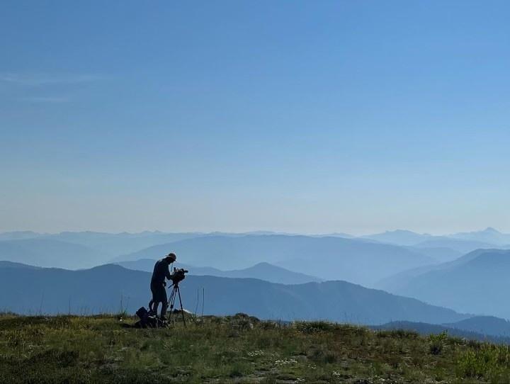 Man with video camera looking off into the distance where there are outlines of mountains