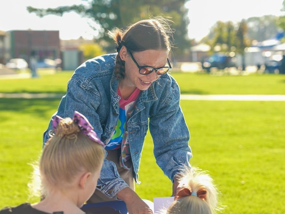 A young woman assisting kids at a craft booth outside