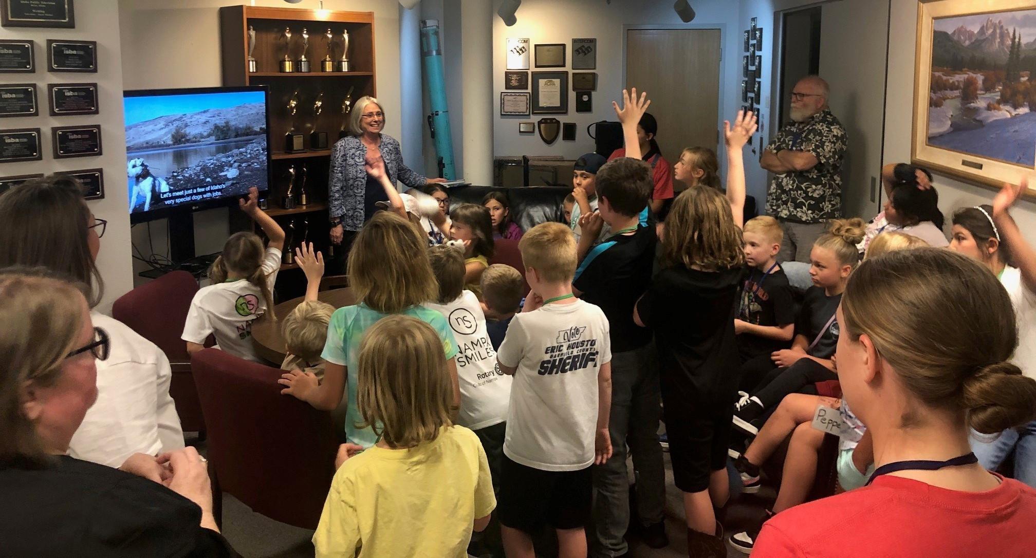 A group of kids are gathered around IdahoPTV host Marcia Franklin