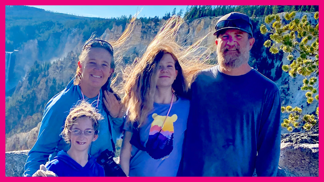 Family of four standing in a windy area outdoors, mother, father and two children all smiling