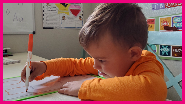 Child drawing while sticking his tongue out and concentrating