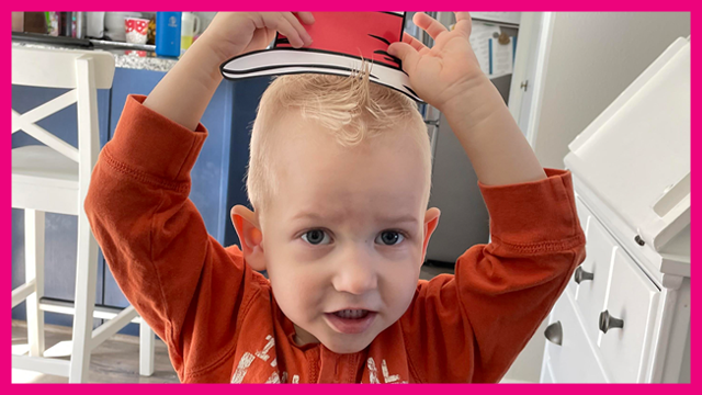 A small boy with blonde hair is raising his arms to put on a hat from 'Cat in the Hat'