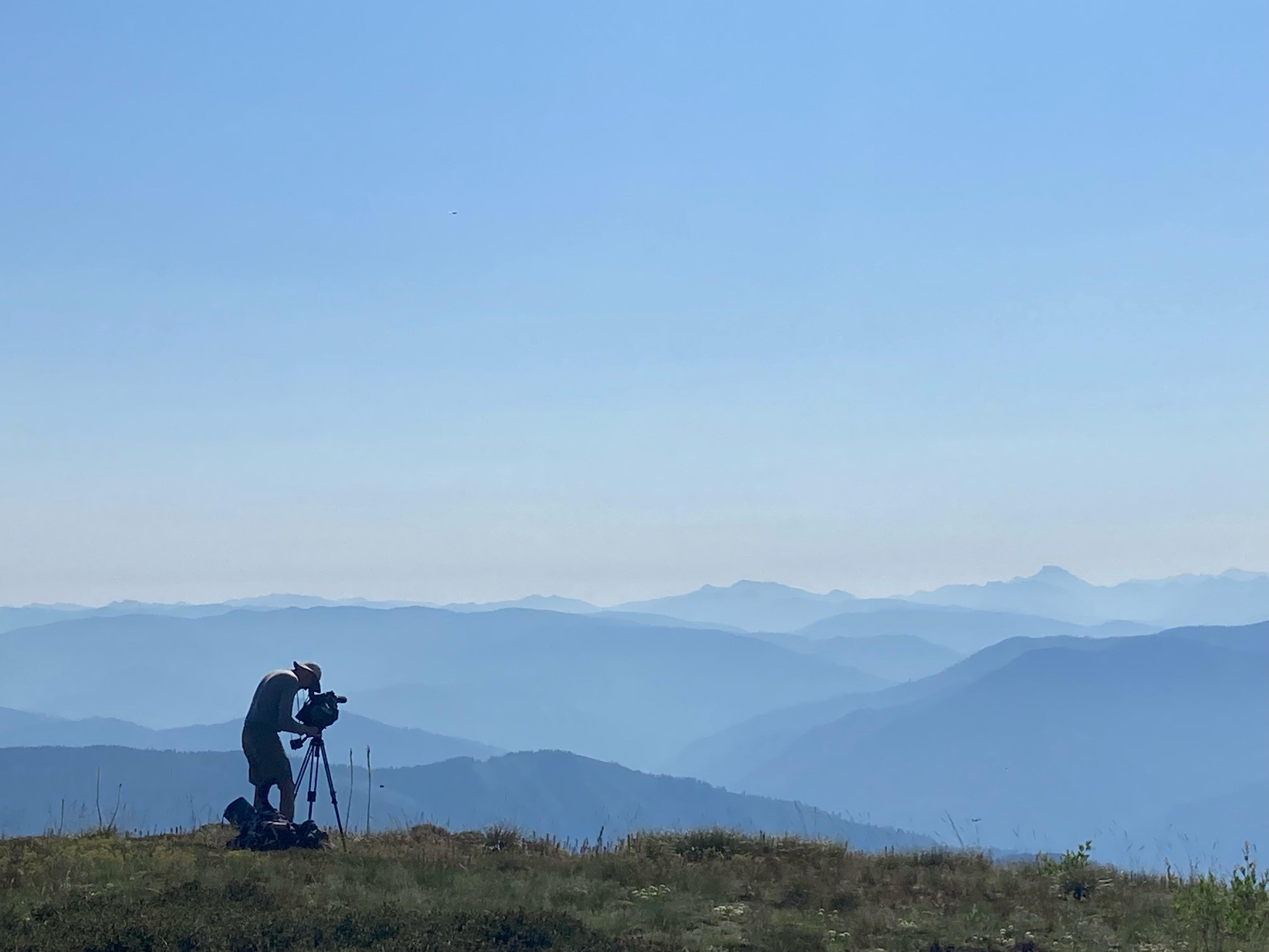 Jay Krajic looking into his camera with a gradient of the mountains behind him