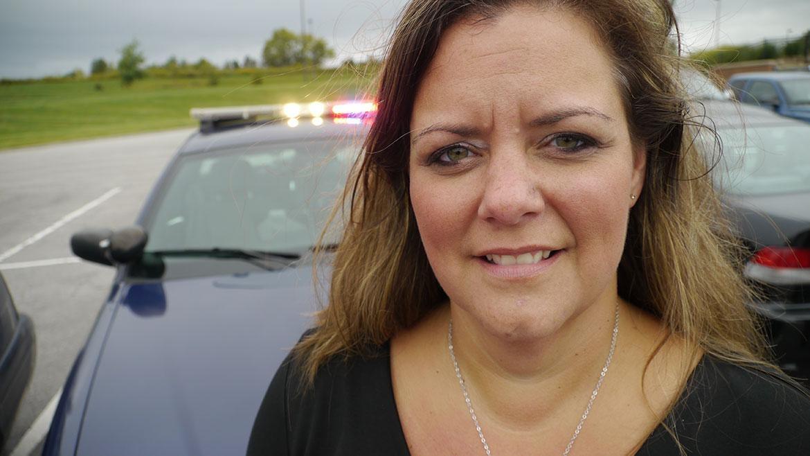 Photo of a woman smiling in front of a police car