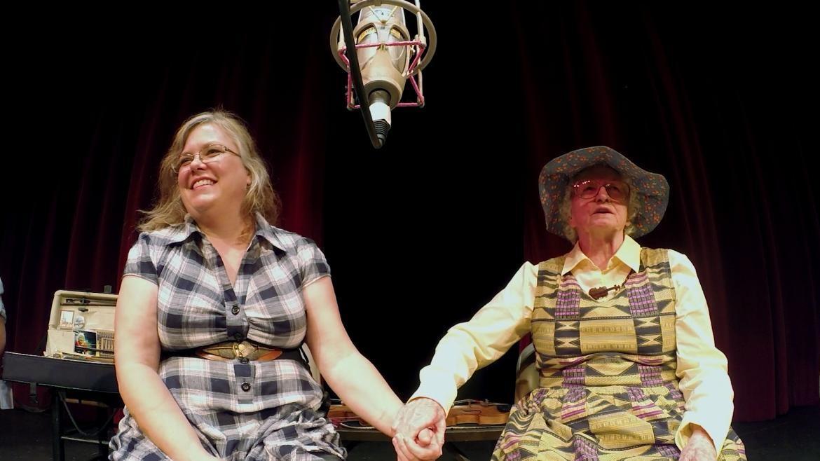 Two women hold hands on stage after a performance