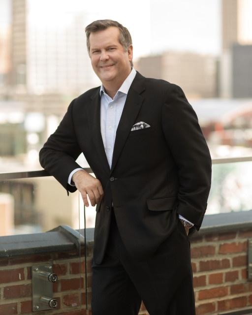 Photo of a man in a suit standing against a wall with Kansas City in background