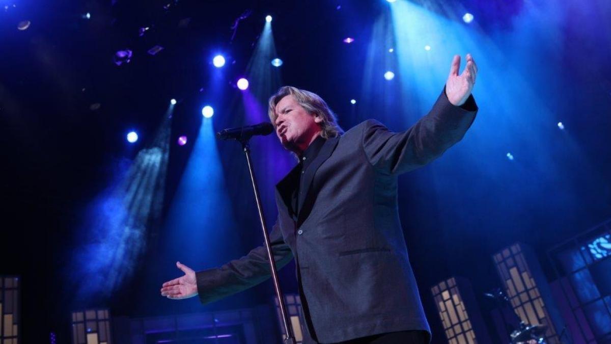 Man stands on stage signing with arms wide open