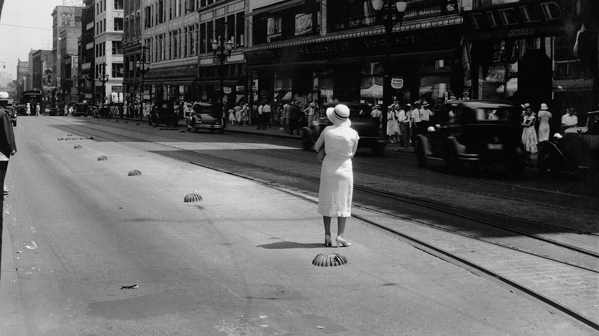Black and white photo of a woman standing in the middle of a street