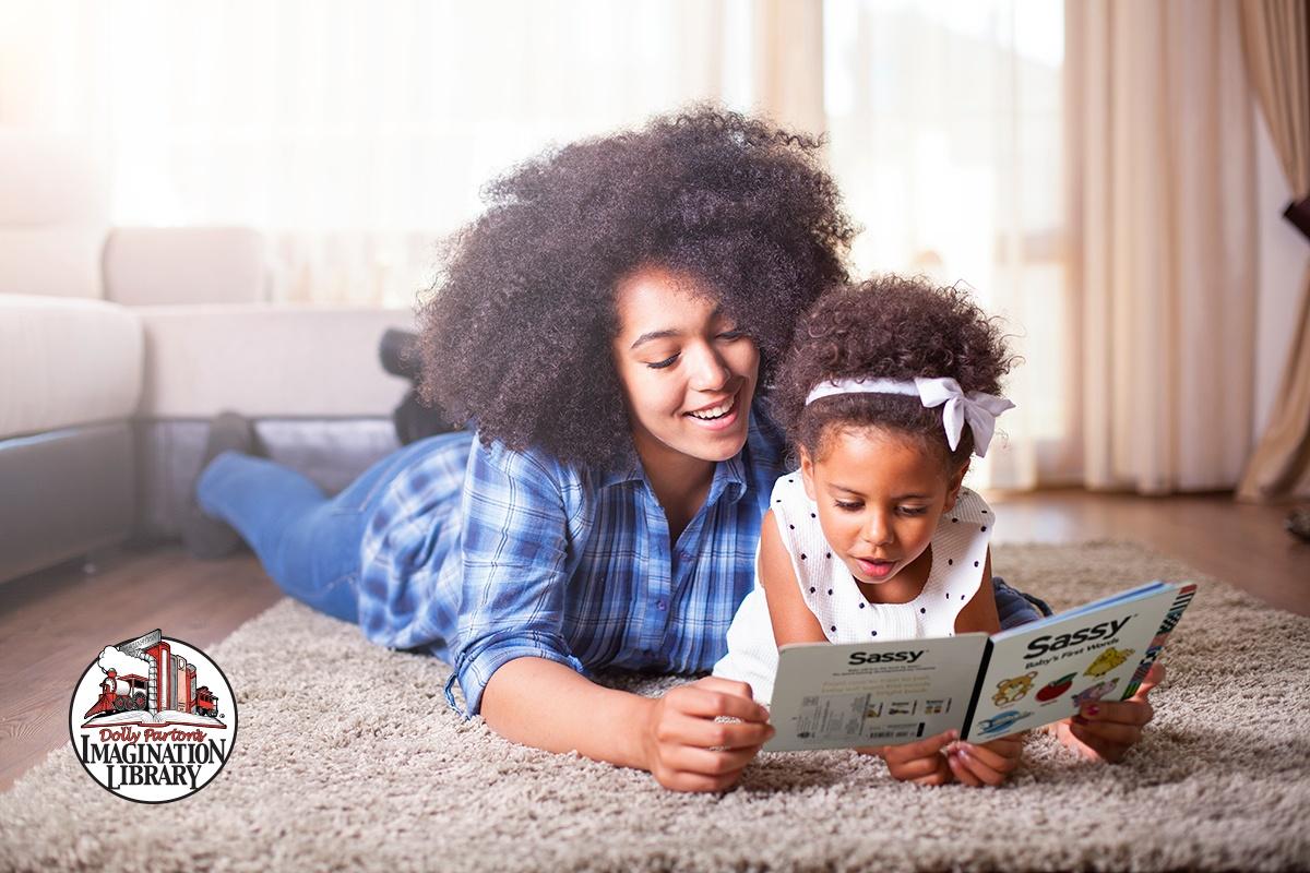 Woman and young girl laying on carpet reading together.