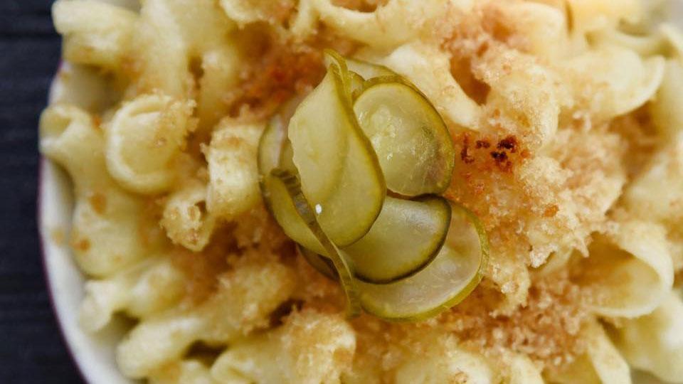 Picture of macaroni and cheese in a bowl with bread crumbs and pickle slices on top