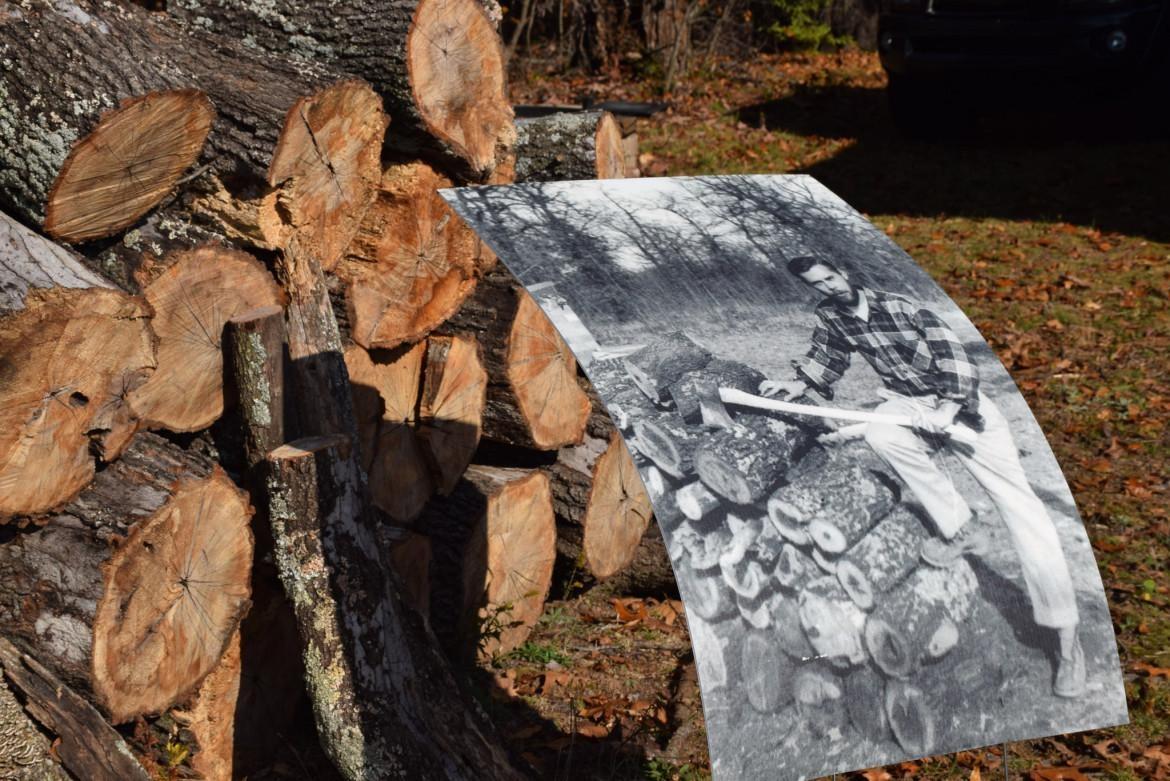 Old printout of a photo of a man chopping wood. Photo printout is resting against a pile of wood. 