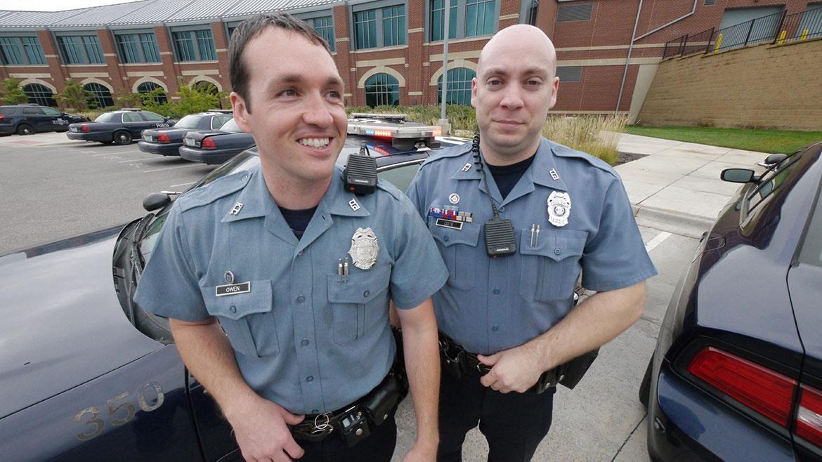 Photo of two police officers in uniform standing in front of police cars