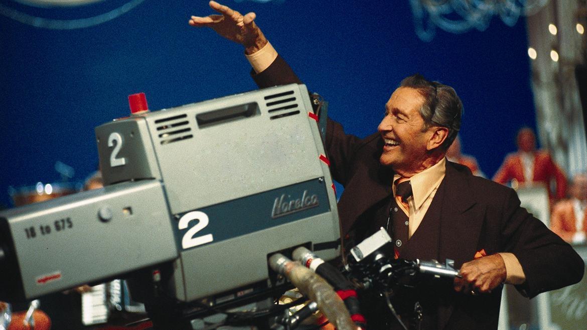 Photo of a man smiling while filming with a large camera
