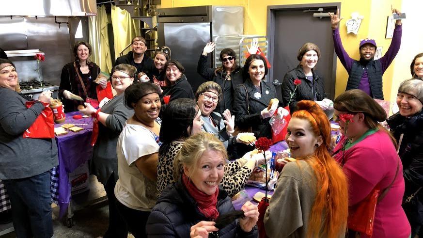 Group of people in a kitchen making PB&J sandwiches.