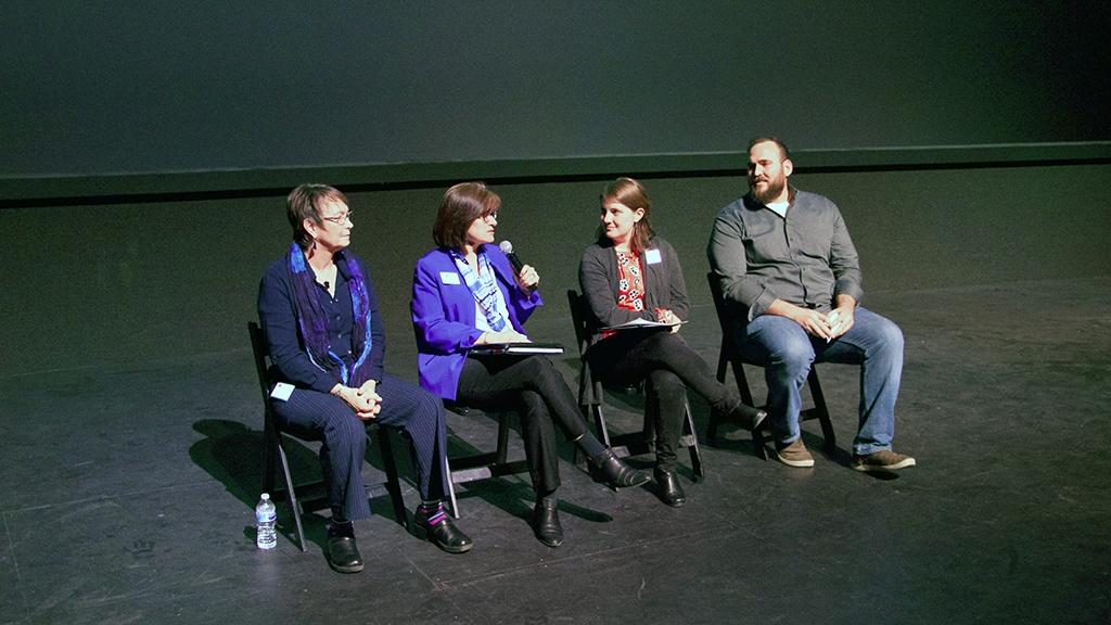 Four people sit on a stage talking with a microphone