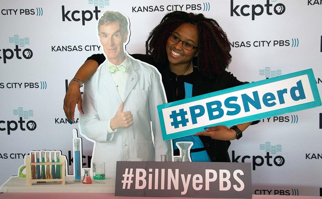 Woman poses with Bill Nye cutout and #BillNyePBS and #PBSNerd signs