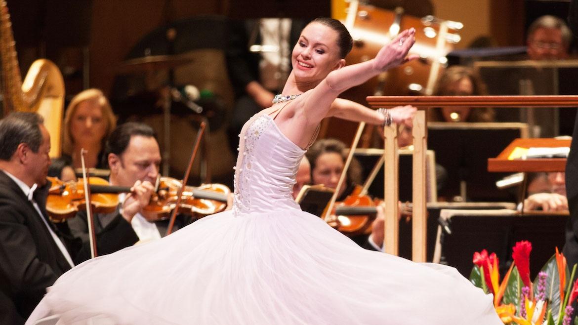 Young ballerina dances on a stage as orchestra plays in the background
