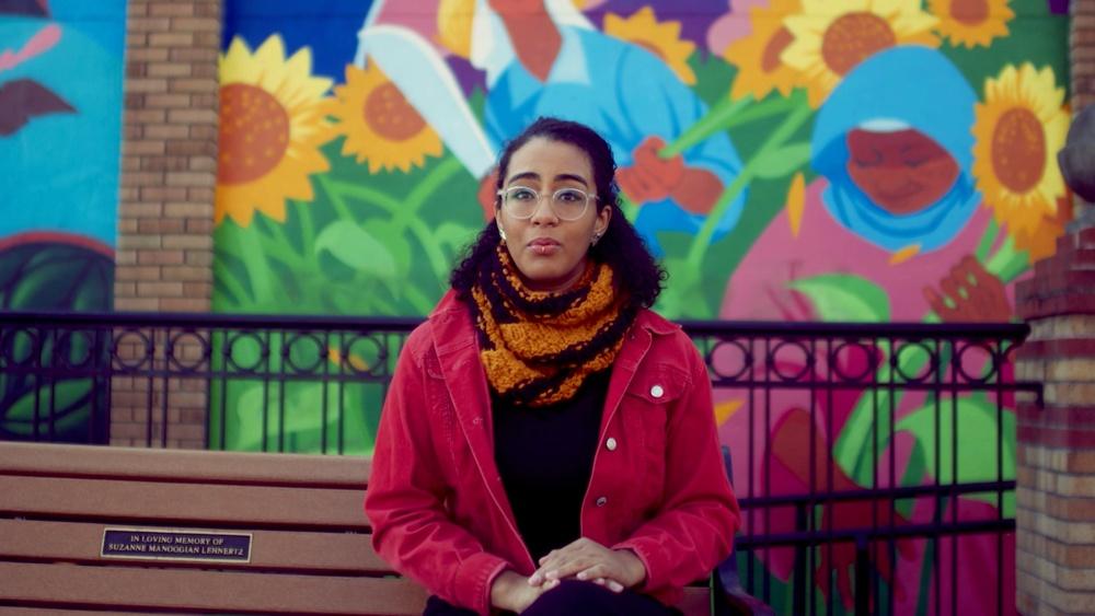 Emily Alvarez on bench with bright sunflower mural in background