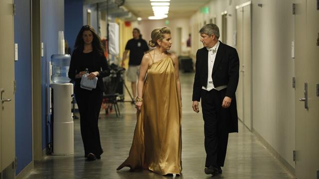 Photo of a woman in a long, gold dress and man in a suit walking down a hall and talking