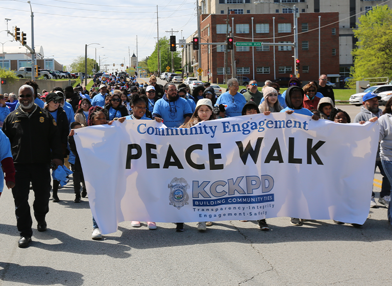 Group of citizens marching holding banner reading Community Engagement Peace Wall KCKPD