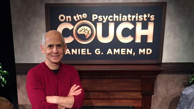 Man smiles in front of sign that reads "On the Psychiatrist's Couch"