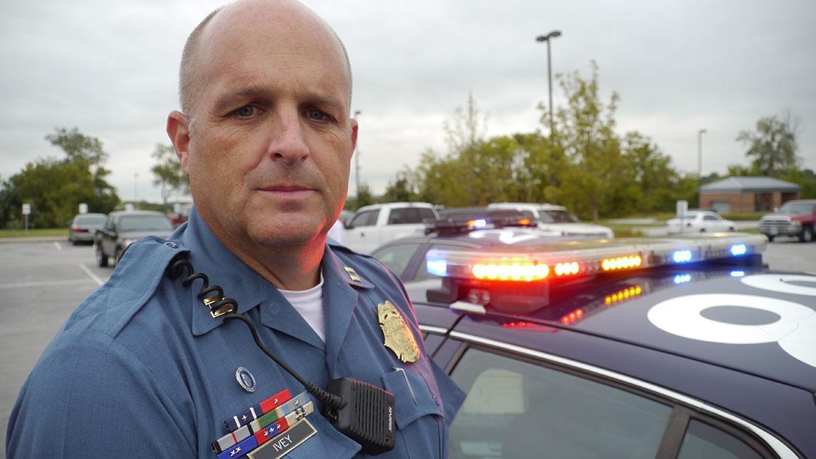 Photo of a male police officer in uniform by his police car