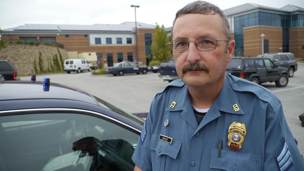 Photo of a male police officer in uniform in front of a police car