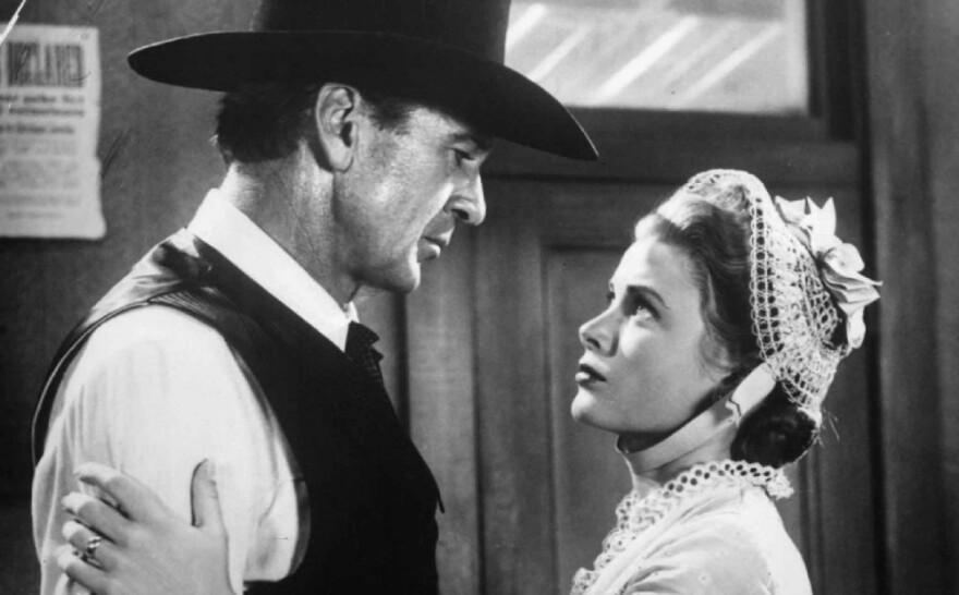 Black-and-white scene from High Noon with Gary Cooper in a cowboy hat and vest holding Grace Kelly in a lace bonnet, both looking serious.